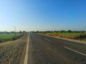 Road amidst field against clear sky