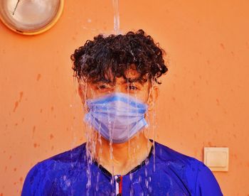 Portrait of man wearing mask taking shower against wall