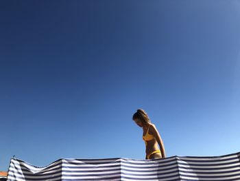 Low angle view of woman standing against clear blue sky