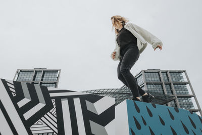 Low angle view of woman balancing on graffiti wall against sky