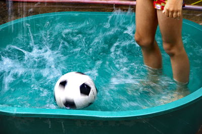 Low section of woman with soccer ball standing in wading pool