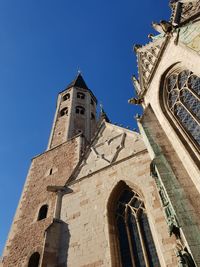 Low angle view of cross amidst buildings against clear blue sky