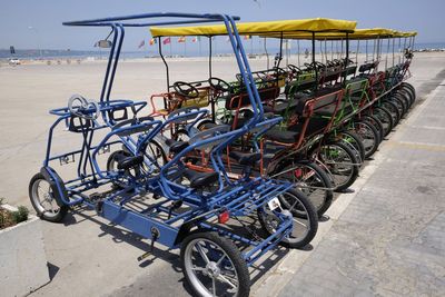 Pedicabs parked by footpath at beach during sunny day