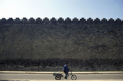 Man riding tricycle on road against abandoned brick wall