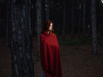 Woman standing by tree trunk in forest