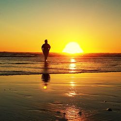 Silhouette man standing on beach against orange sky