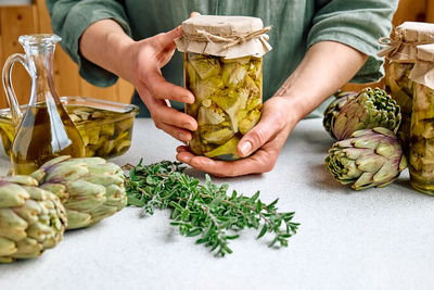 Artichoke hearts marinated with olive oil and herbs.woman holding glass jar with pickled artichokes.