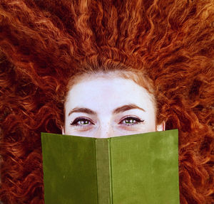 Directly above shot of redhead woman holding book while lying on field