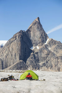Climber sitting in tent below large beautiful mountain summit.