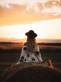 Rear view of woman sitting on field against sky during sunset