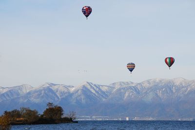 Hot air balloon flying over lake against clear sky and snowy mountains