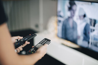 Midsection of teenage girl holding remote controls by television set in living room at home