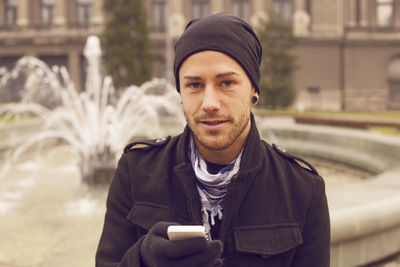 Man using mobile phone while sitting against fountain