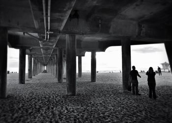 People on beach below view of an empty bridge