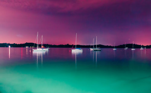 Sailboats moored on sea against sky at night