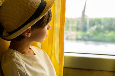 A boy in a hat looks out the window thoughtfully while sitting on a tour bus