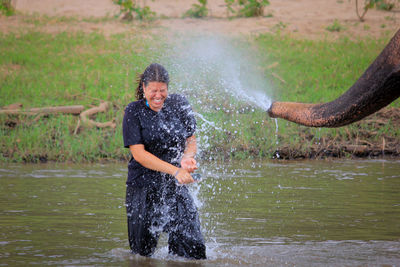 Cropped trunk of elephant spraying water on woman in river