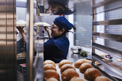 Woman holding food in tray by oven at bakery