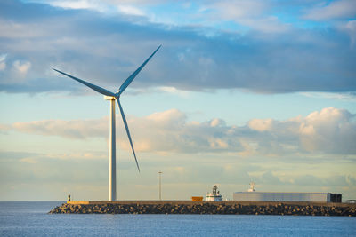 View of sea bay and large windmill at edge of stone breakwater