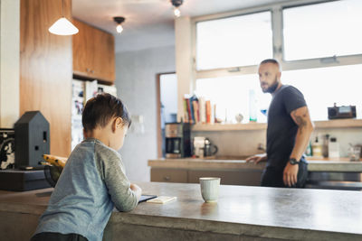 Father looking at son using digital tablet in kitchen