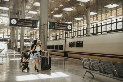 Mother walking with baby stroller and wheeled luggage at train station