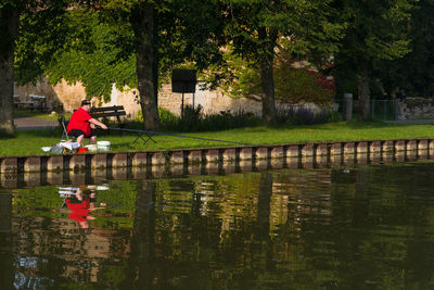 A retired fisherman fishes fish in a canal. view of man with umbrella fishing by trees. 