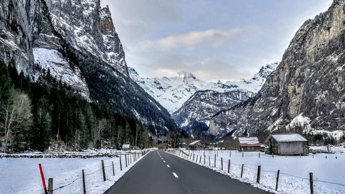 Snow covered road by trees against sky