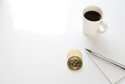 High angle view of coffee cup with bitcoins on white background