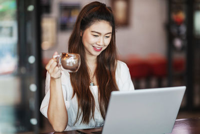 Smiling woman using laptop while having coffee at cafe