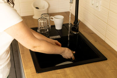 Female hands, a young woman washes cutlery in the sink in the kitchen, washing dishes
