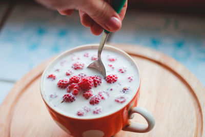 Close-up of hand stirring milk and berries in cup