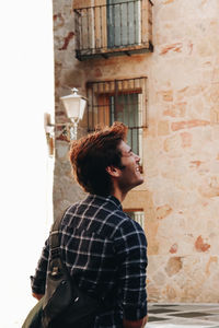 Side view of young man standing against building