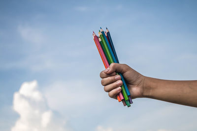 Close-up of hand holding multi colored umbrella against blue sky
