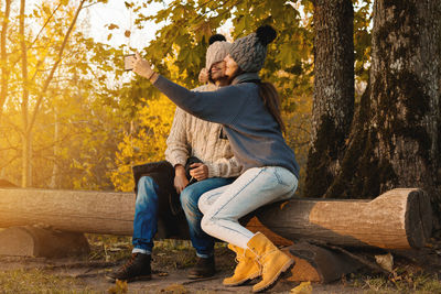 Couple taking selfie while sitting on log