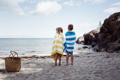 Boy and girl stood on the beach wrapped in towels looking at the ocean