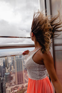 Side view of fashionable woman with tousled hair standing by window in city