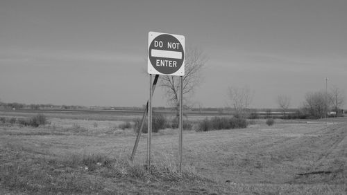 Road sign on field against sky