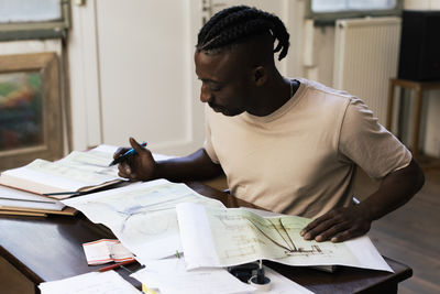 Focused male architect analyzing blueprints at table in workplace