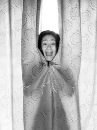 Portrait of scared woman shouting while standing against curtain