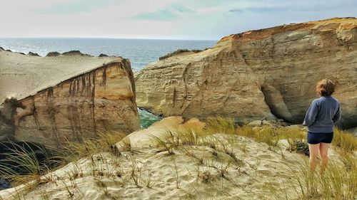 Rear view of woman standing on rocks at seaside