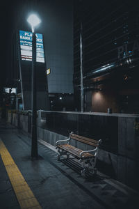Empty road by illuminated buildings in city at night