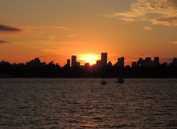 Silhouette buildings by sea against sky during sunset