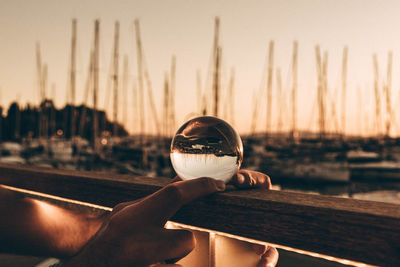 Reflection of person hand on glass against sky during sunset