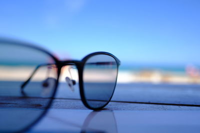 Close-up of eyeglasses on beach against blue sky