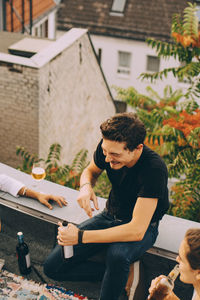 High angle view of happy man enjoying beer while sitting with friends on terrace at party