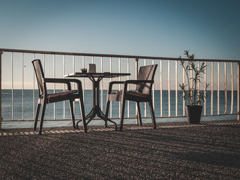 Chairs and tables at beach against clear sky