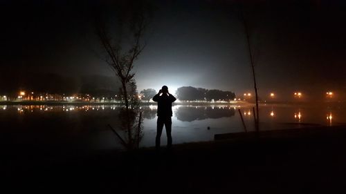 Silhouette man standing by lake against sky at night