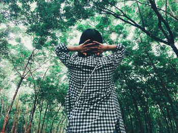 Rear view of woman with hands behind head standing against trees in forest