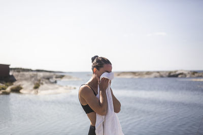 Woman cleaning face with towel against sea