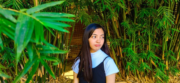 Portrait of beautiful young woman standing against plants